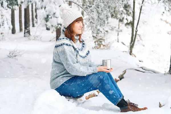Женщина с чашкой чая в руках сидит в заснеженном лесу — стоковое фото
