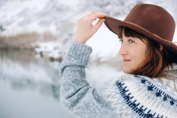 Portrait of a woman in a felt brown hat and sweater on a background of winter landscape — стоковое фото