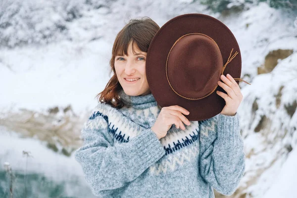 Портрет улыбающейся женщины в коричневой шляпе и свитере на фоне зимнего пейзажа — стоковое фото