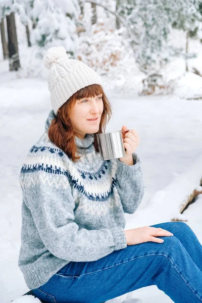 Winter woman portrait with a cup of tea in her hands siting in in snow-covered forest. Copy, empty space for text — стоковое фото