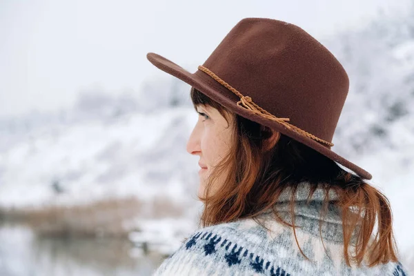 Portrait of a woman in a felt brown hat and sweater on a background of winter landscape — стоковое фото