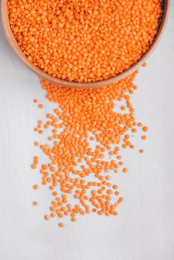 Beyaz bir masada tahta bir kasede çiğ kırmızı mercimek..