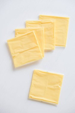 Beyaz ahşap masa arkasında ayrı paketlenmiş peynir dilimleri.