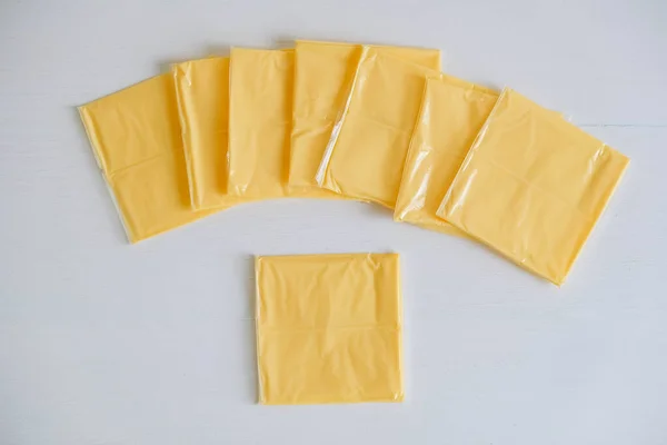 Fatias de queijo embaladas separadamente em um fundo de mesa de madeira branca — Fotografia de Stock