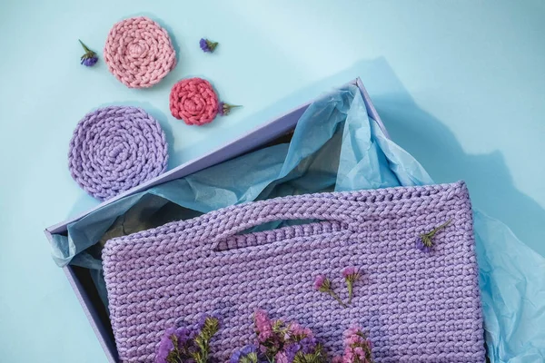 Handmade purple knitted bag in a paper box on a blue background