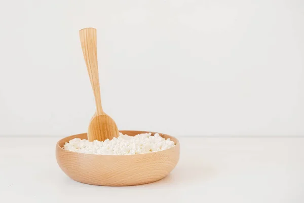 Fromage cottage dans une assiette en bois avec une cuillère sur fond blanc — Photo