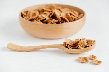Crispy healthy dry cereal flakes in a wooden bowl with wooden spoon on white background.