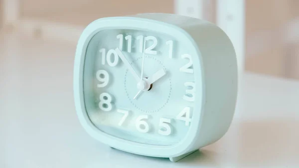 Blue table clock with arrows on a white table.