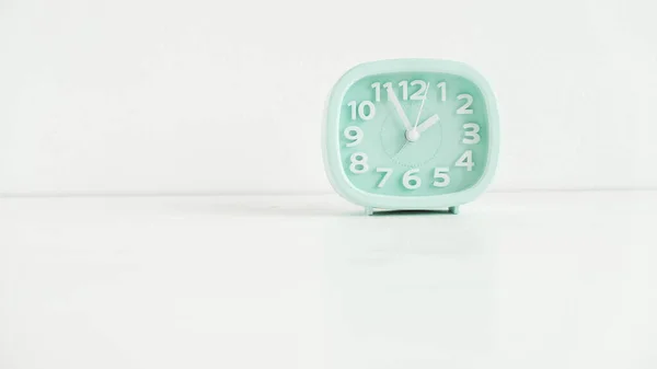 Blue table clock with arrows on a white table.