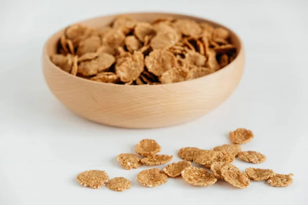 Crispy healthy dry cereal flakes in a wooden bowl on white background.