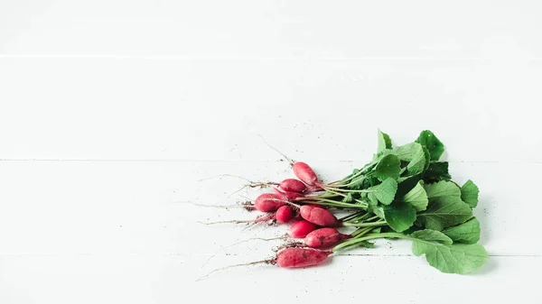 Fresh bunch of radishes on a white wooden background.