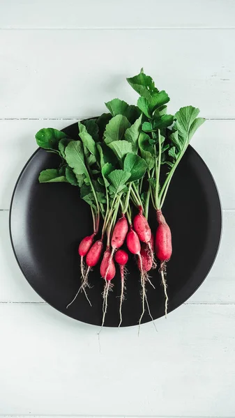 Bunch of radishes in a black plate on a white wooden background.