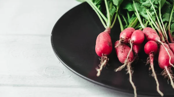 Bunch of radishes in a black plate on a white wooden background.