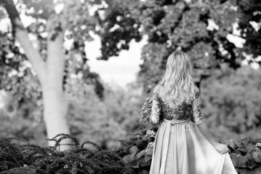 Gri zarif elbiseli genç sarışın kız, arkadan manzaralı, parkta bir buket pembe çiçekle. Rahat ol. Sonbaharda parkta dinlenin. Moda ve güzellik konsepti.