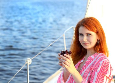 Elinde bir bardak kiraz tutan ve kameraya gülümseyen genç bir kadının olduğu pankart. Arka plan mavi deniz. Seyahat ve eğlence. Uzayı sola kopyala.