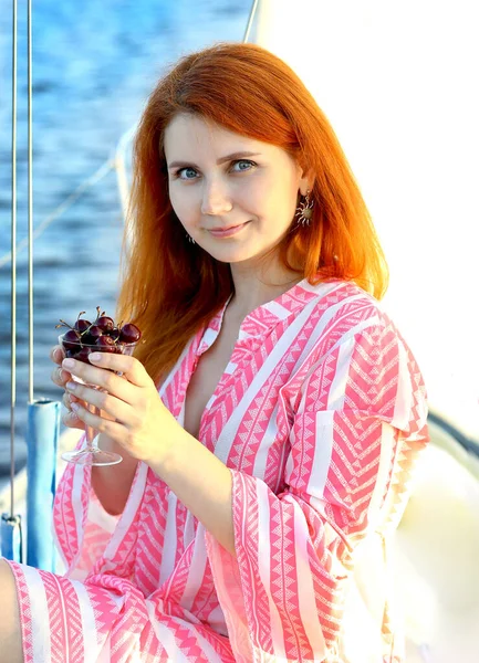 Pembe elbiseli, gülümseyen, tatile çıkmış, kirazlı genç bir kadın. Arka plan mavi deniz. Seyahat ve tatil kavramı.