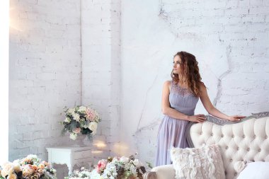 Arka planı olan bir pankart. Pencereden gelen güneş ışınları. Modern iç tasarım konsepti. Kanepenin yanında duran lavanta rengi elbiseli genç bir kız. Çiçek dekoru. Uzayı sola kopyala