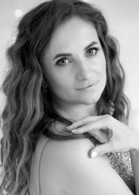 black and white portrait of a stunning young brunette girl in a half turn, hand on shoulder, in a lavender color dress. Looking into the camera. Modern make-up, beautiful blue eyes, hairstyle. Fashion