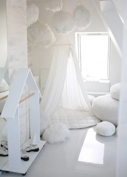 Cozy white children\'s room on the attic floor. Tepee-tent with a rug, a pillows. Decor with clouds on the ceiling.