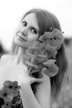 Siyah elbiseli, elinde kırmızı haşhaş buketi olan güzel bir kızıl saçlı kadının çarpıcı siyah beyaz portresi. Çiçekler. Yaz. Moda ve güzellik konsepti. 