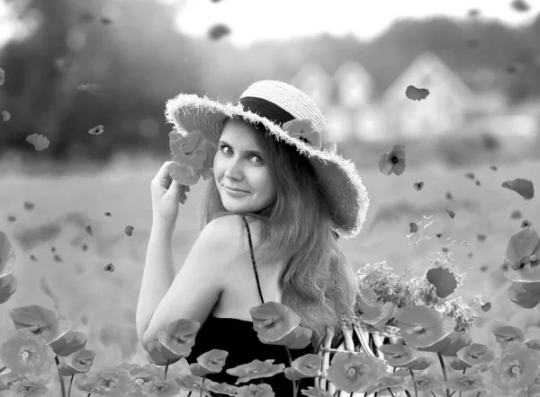 black and white portrait a girl in a black dress and a hat holding red poppies. Beautiful poppy field and landscape of sunset in the background. Copy space. Summer concept