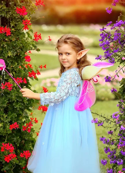 Little elf girl in a blue dress with wings and a magic wand in the park. Magic. Childhood. Summer concept