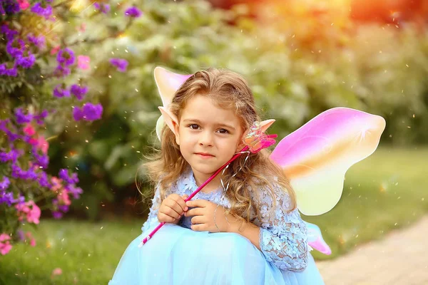 Sad little elf girl in a blue dress with wings in the park. Summer. Children concept