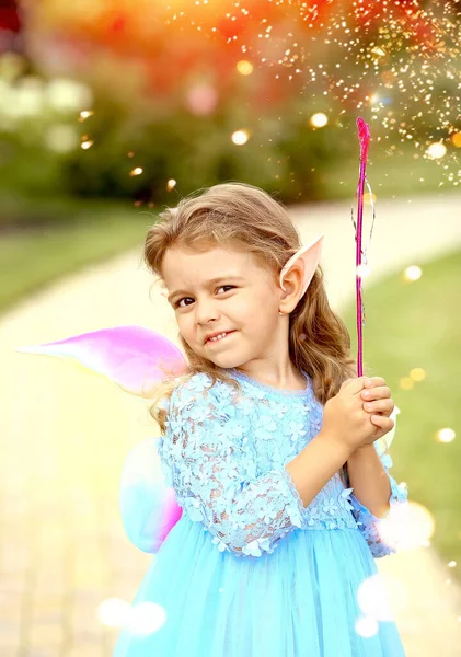 Little elf girl in a blue dress with wings plays magic in the park. Summer. Childhood concept