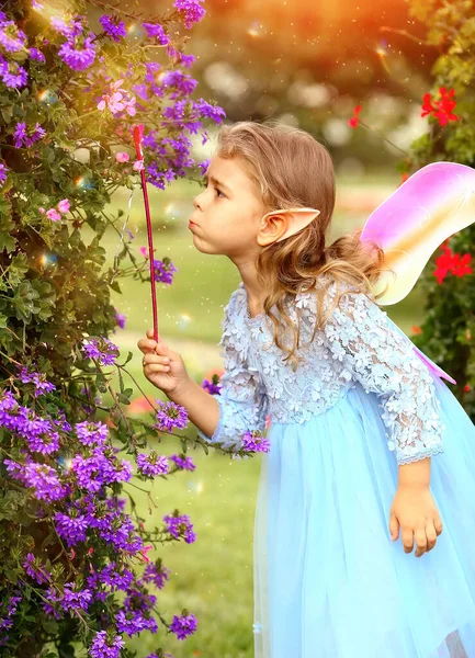 Little elf girl in a blue dress with wings plays magic in the park. Childhood. Summer concept