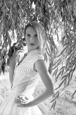 Siyah beyaz bir portre. Puantiyeli bir elbise giymiş beyaz bir kız. Kameraya kendinden emin bir şekilde bakıyor. Güneşli bir gün. Yaz. Nehir arka planı. Moda ve güzellik konsepti.