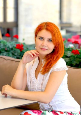 Beyaz bluzlu esmer ve beyaz etekli çekici bir kızın göz kamaştırıcı portresi ve gül desenli etekli yaz kafesinde oturan çiçeklerle dolu oyun parkı. Kentsel yaz geçmişi. Kadın konsepti