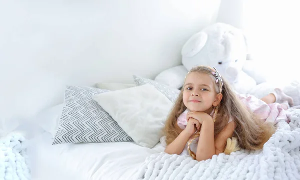 Banner with a little cute girl with a smile lies on the bed. Bright interior in the children\'s room. Scandinavian interior style. Happiness concept. Copy the space on the left