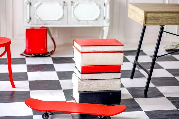 School supplies. A stack of books, a skateboard, a red backpack and an exercise table. Back to school. Education concept.