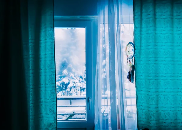 View from the window with blue curtains and dreamcatcher. Winter day.