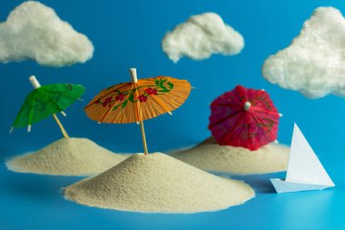 Kumda kokteyl, kağıttan tekne ve sahilde beyaz bulutlar için kağıt şemsiyeler. Kopyalama alanı olan yaratıcı yaz konsepti.