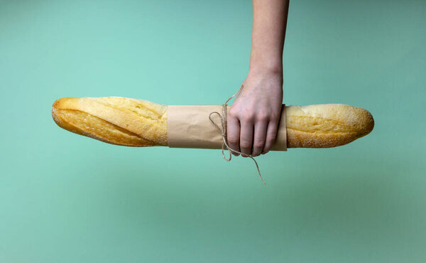 Рука держит свежий багетный хлеб, завязанный ремесленной бумагой с бечевкой на зеленом фоне. Концепция здорового питания. Копирование пространства.