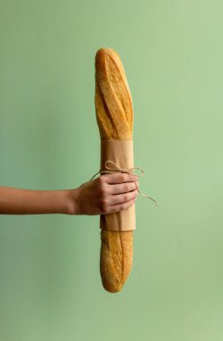 Bir el yeşil arka planda taze bir baget ekmeği tutar. Sağlıklı bir yaşam tarzı. Boşluğu kopyala.