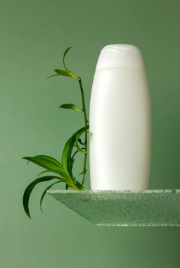 Cam bir podyumda beyaz şişe ve yeşil bitki yapraklarıyla moda bir kompozisyon. Organik kozmetik ürünlerle dekoratif podyum. Yüze güzellik bakımı kavramı.