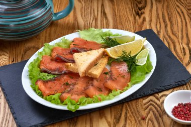Limon ve limonla kesilmiş somon balığı, beyaz tabakta salata ve kızarmış ekmek.