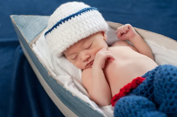 Een week oud pasgeboren babyjongen slapen op zijn rug in een kleine boot. — Stockfoto