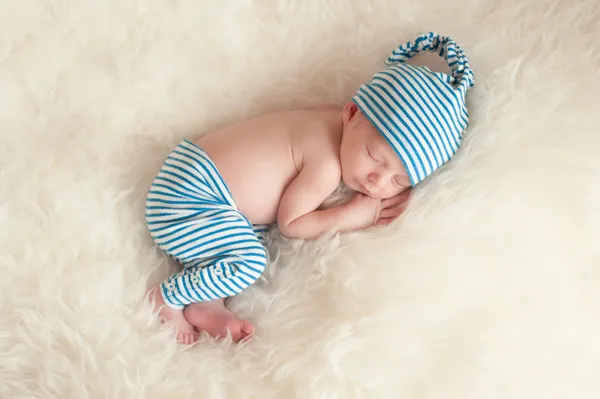 Bebê recém-nascido vestindo pijama listrado azul e branco e dormindo em pele de falso branco . — Fotografia de Stock