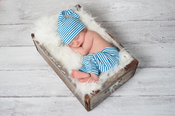 Pasgeboren baby blauwe en witte gestreepte pyjama dragen en slapen in een vintage, houten, soda pop krat. — Stockfoto