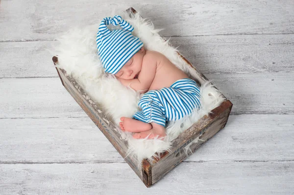 Bebê recém-nascido vestindo pijama listrado azul e branco e dormindo em uma caixa pop vintage, de madeira, refrigerante . Fotos De Bancos De Imagens Sem Royalties