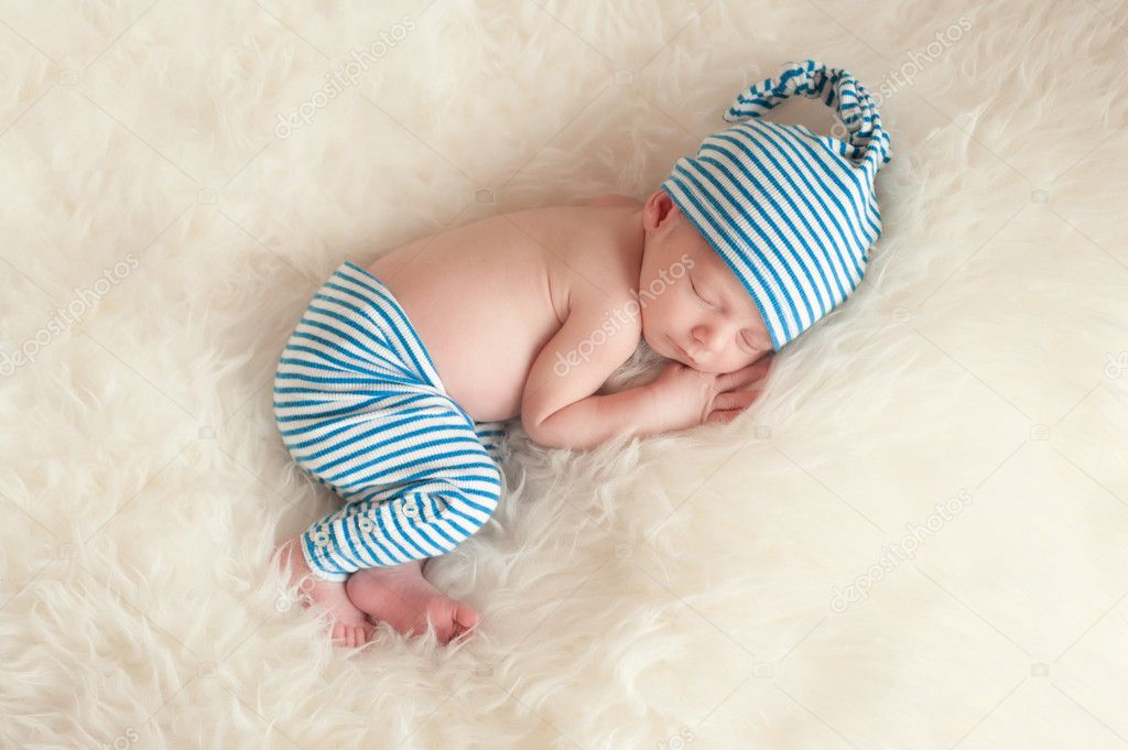 Newborn baby wearing blue and white striped pajamas and sleeping on off white faux fur.