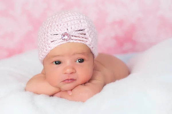 Neugeborenes Mädchen trägt einen rosa gehäkelten Klapphut, stützt sich auf ihre Arme und schaut weg. — Stockfoto