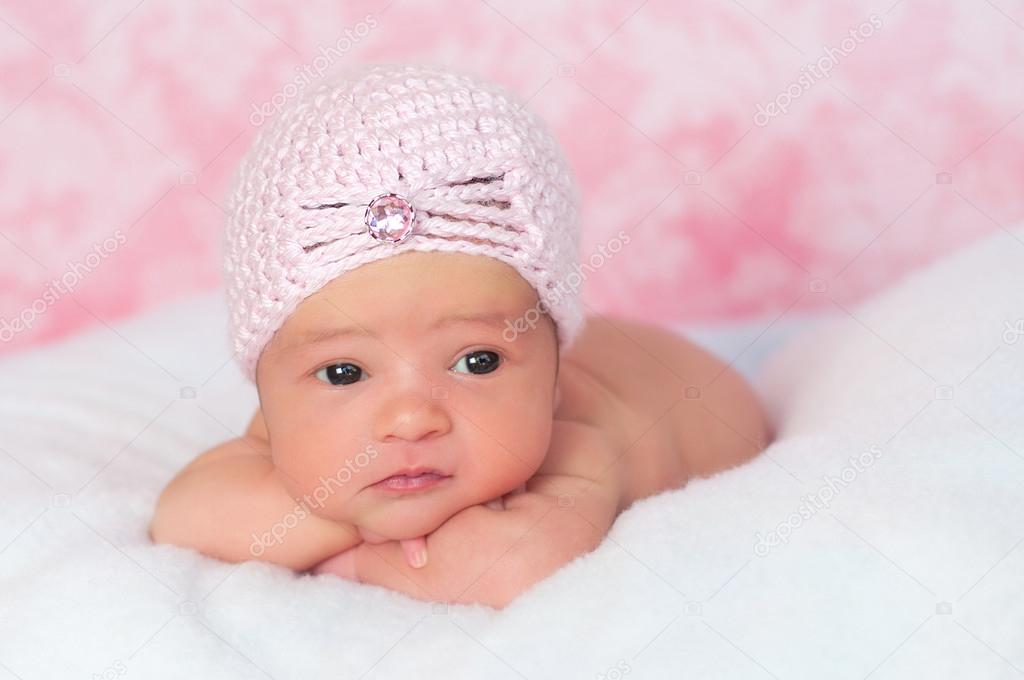 Newborn girl wearing a pink crocheted flapper style hat, propped up on her arms and looking away.