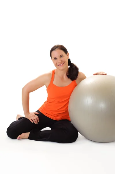 Mujer sonriendo y apoyándose en una bola de ejercicio gris . — Foto de Stock