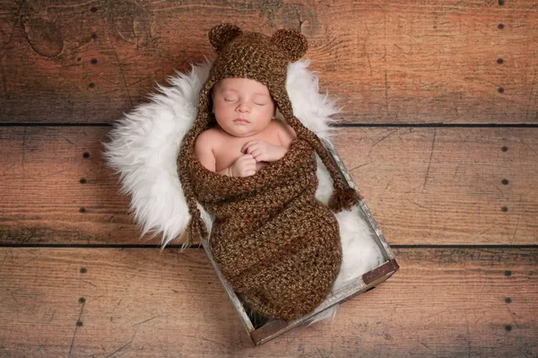 Pasgeboren babyjongen dragen van een hoed bruin gehaakte Beer en slapen in een vintage houten doos. — Stockfoto