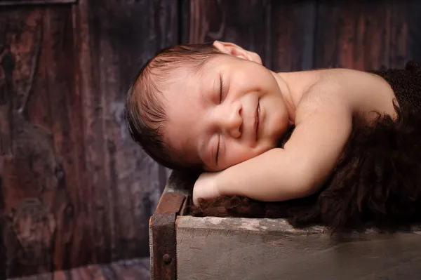 Sorridente neonato che dorme in una cassa rustica — Foto Stock