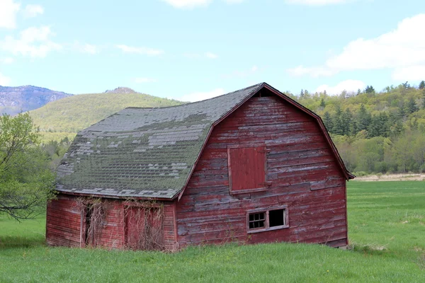 Antiguo granero rojo abandonado en el campo rural con cordillera y cielos azules como telón de fondo —  Fotos de Stock